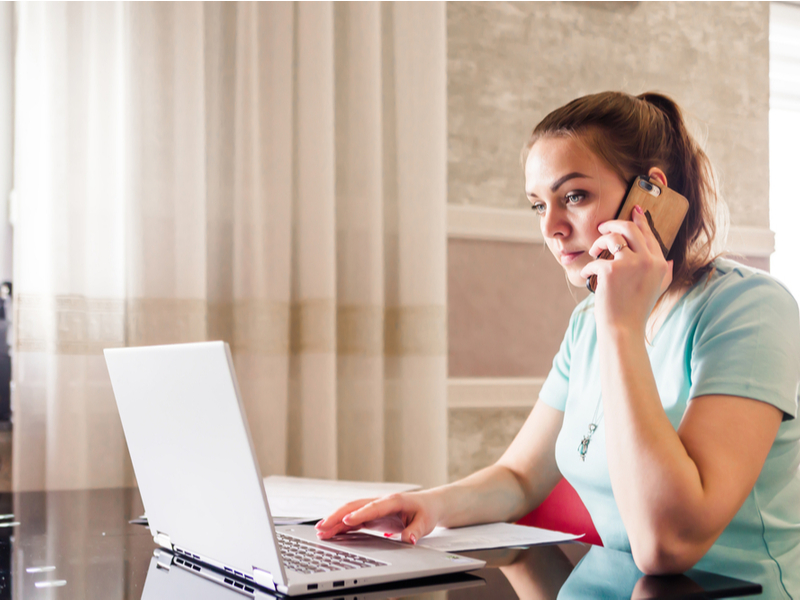 Young woman working from home and talking on smartphone.