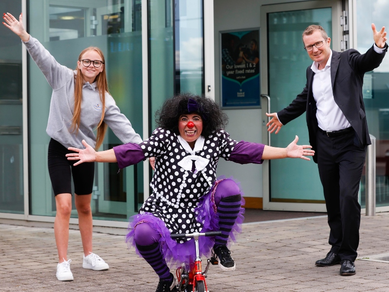 Young woman, woman dressed in clown outfit and man in dark suit.