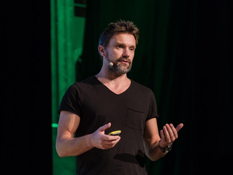 Man in black t-shirt making a presentation on stage.