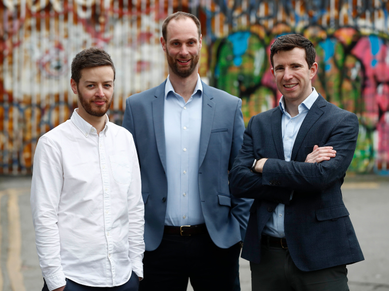 Three men standing in front of graffiti wall.