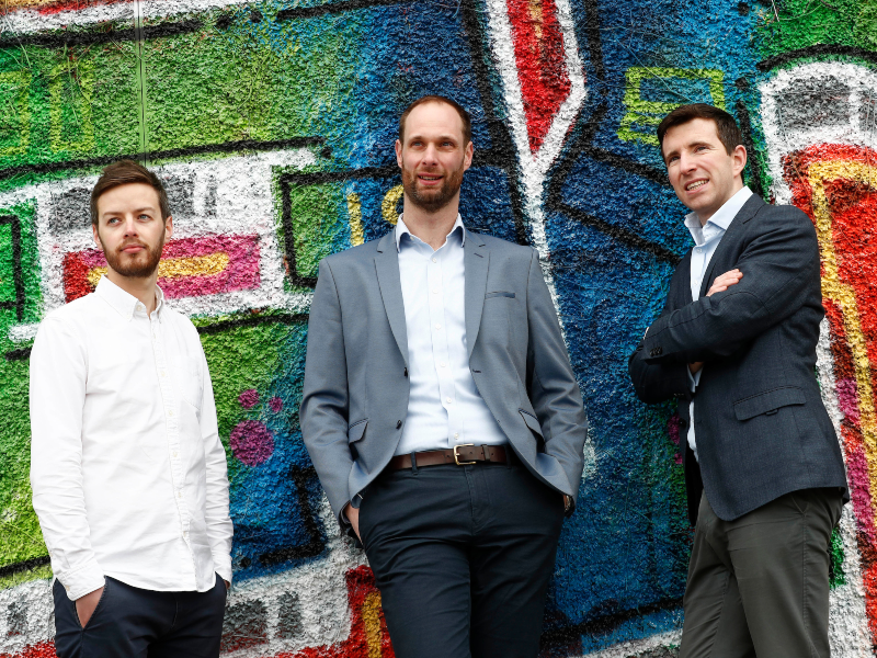 Three men standing next to a graffiti wall.