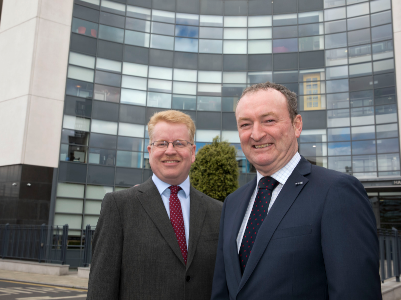Two men in suits standing in front of a glass building.
