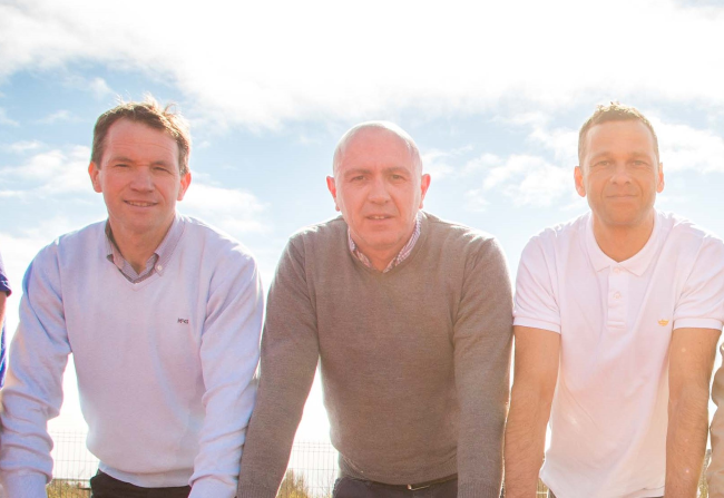 Three men with a cloudy sky behind them.