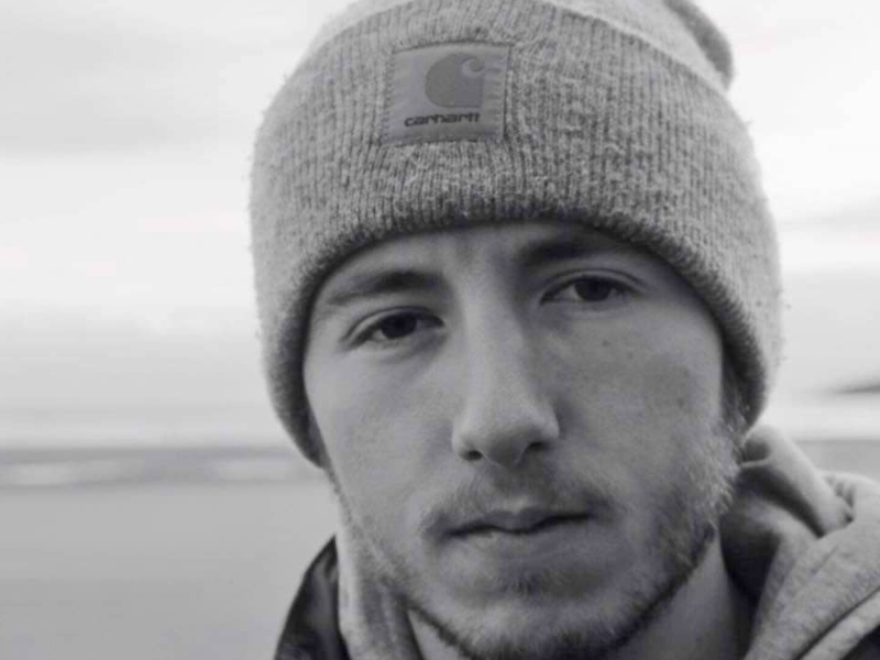 Black and white image of a man wearing a hat on a beach.