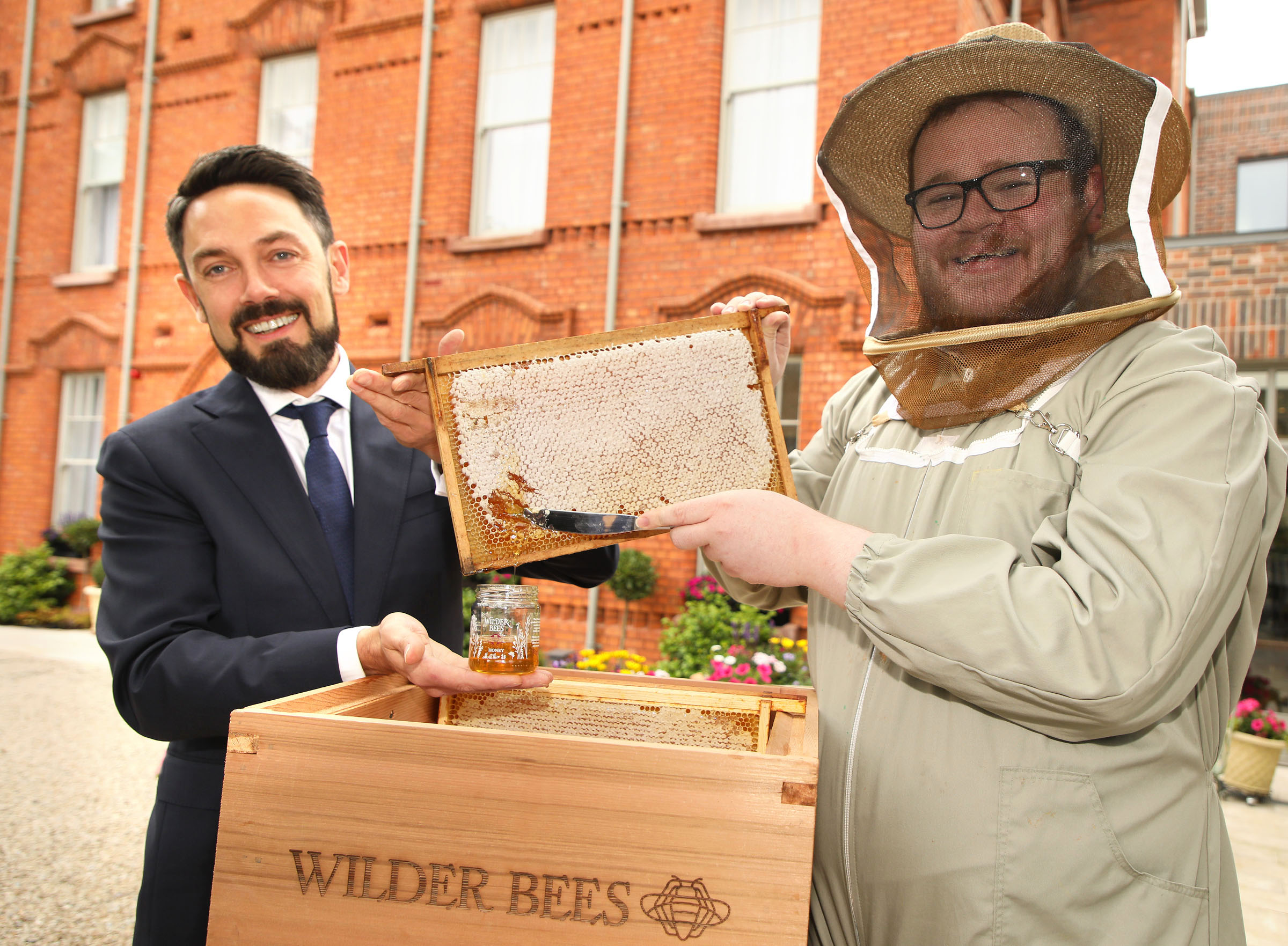 Man in suit beside man in bee suit.