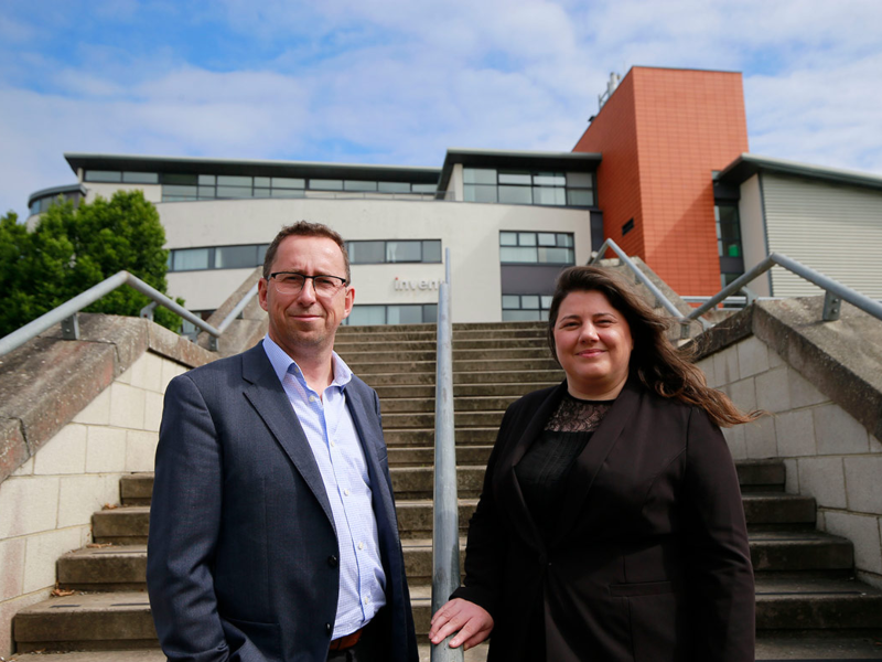 Man in blue jacket and woman in black suit standing outside a building.