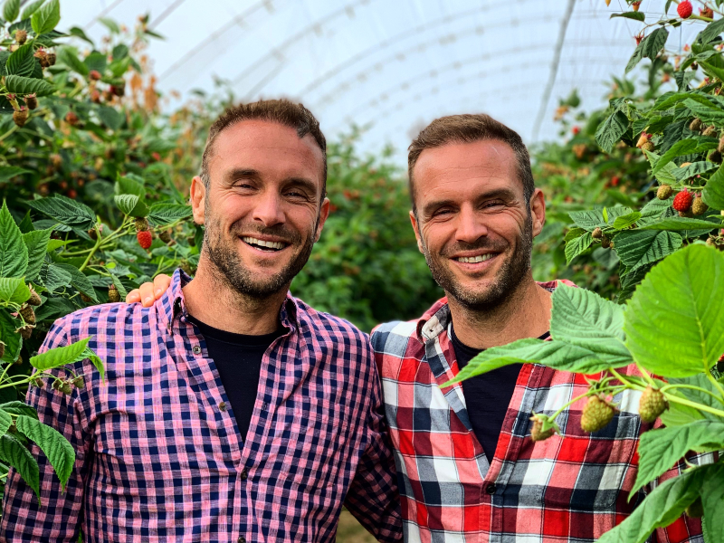 Identical twins in check shirts in a greenhouse.