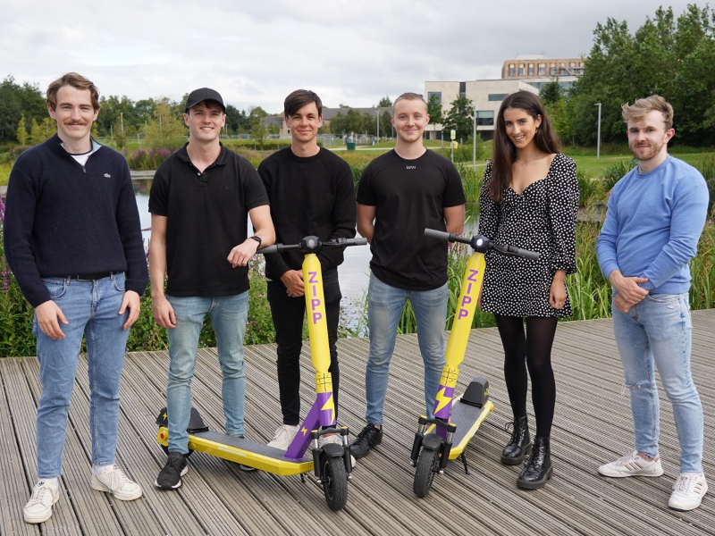 Group of people standing with 2 e-scooters.