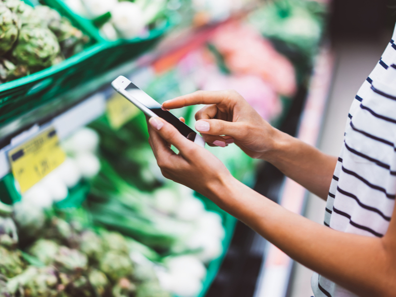 Woman using smartphone while shopping for groceries.