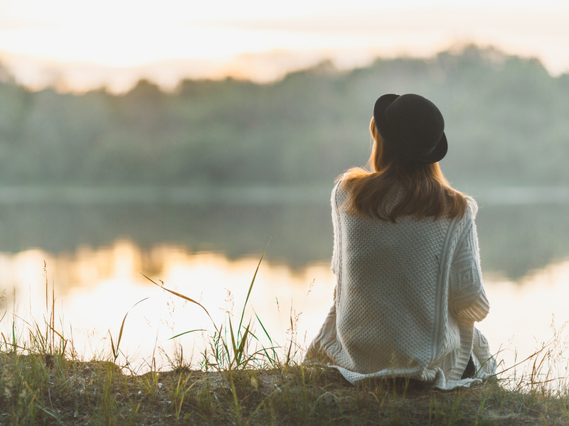 Woman in a hat sitting by a river bank.