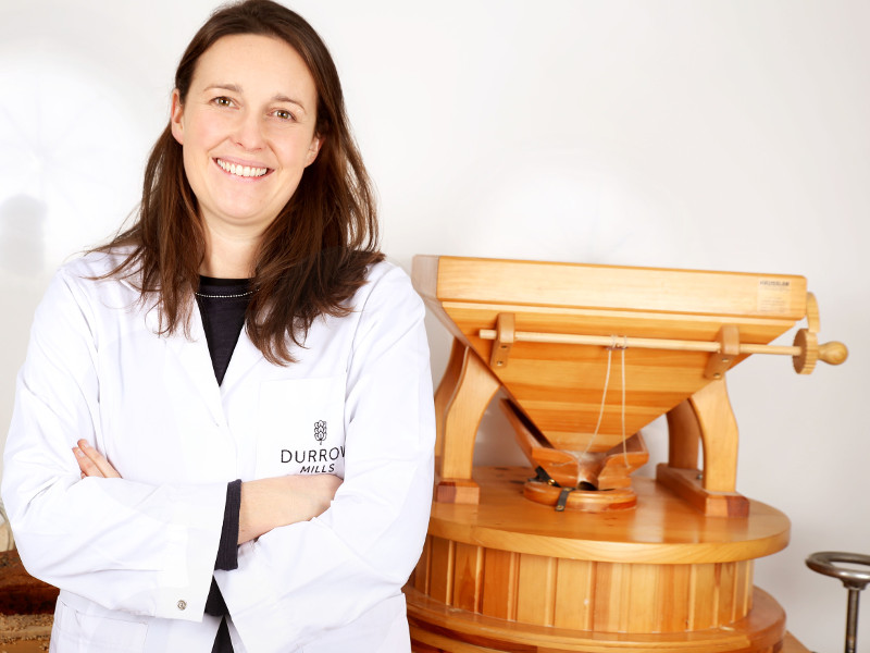 Woman in white coat beside a flour mill.