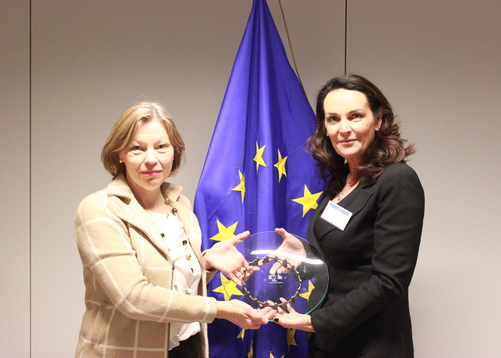 woman in dark jacket receiving an EU award.