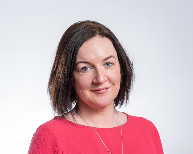 Dark-haired woman wearing pink jumper.