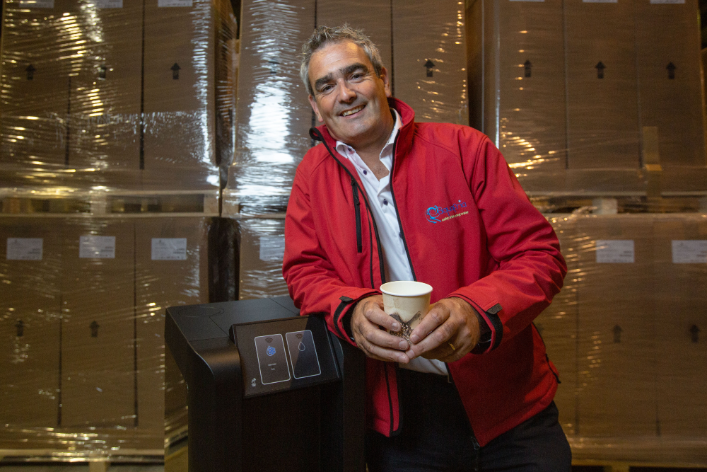 Man in red jacket leaning against water dispenser.