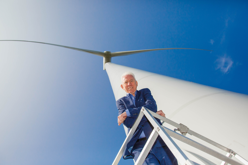 Man standing under wind propeller under a blue sky.