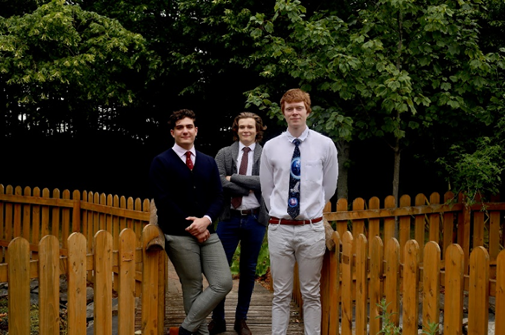 Three young men leaning on a fence.