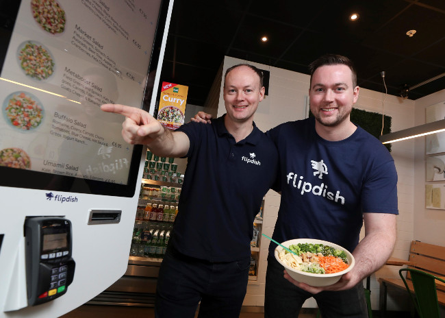 Two men standing beside a food kiosk.