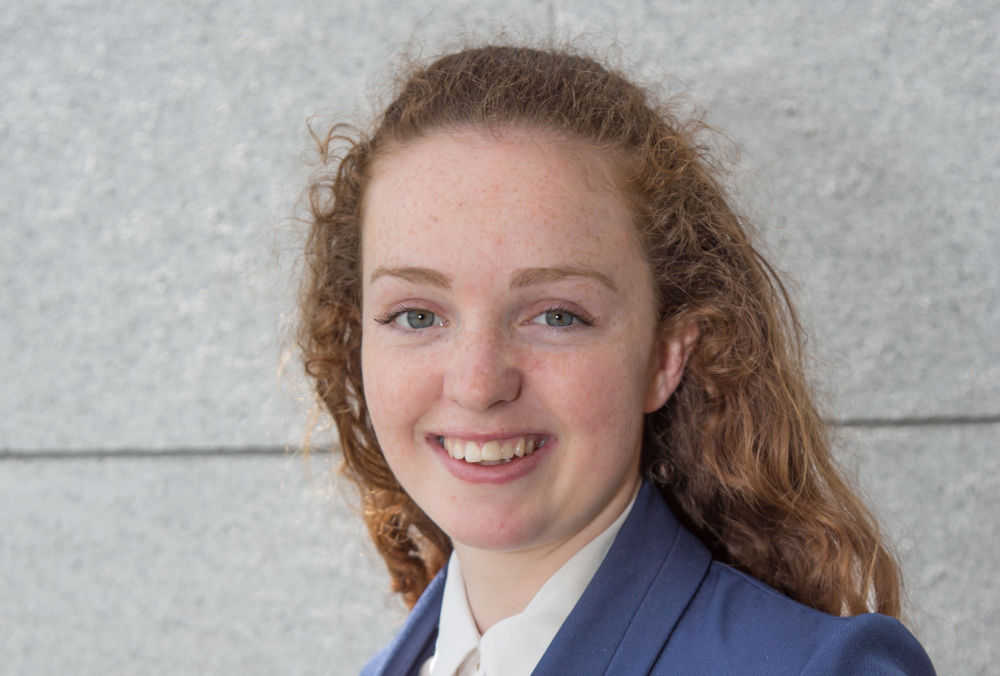 Young woman with red hair and wearing blue jacket and white blouse.