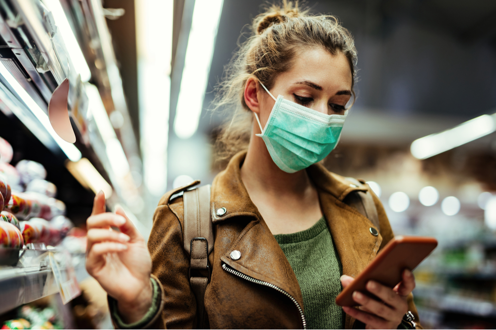 woman in mask in shop looking at phone.