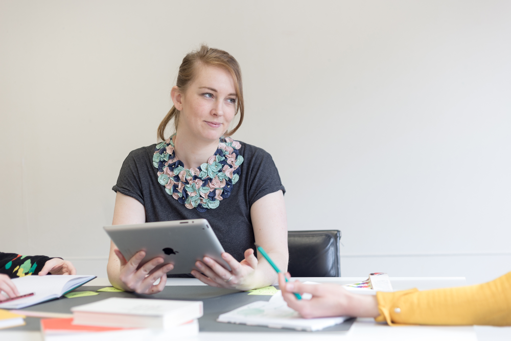 Young woman wearing colourful necklace holding an iPad at a meeting.