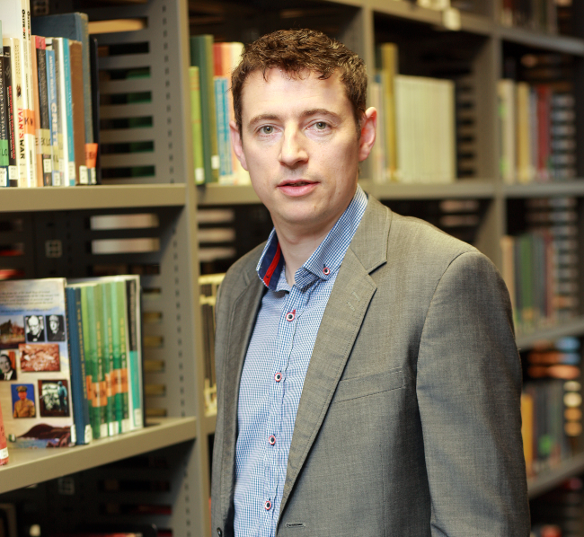 Dark-haired man standing in a library.