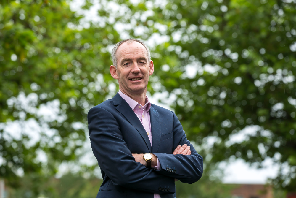 Man in blue suit standing in front of trees.