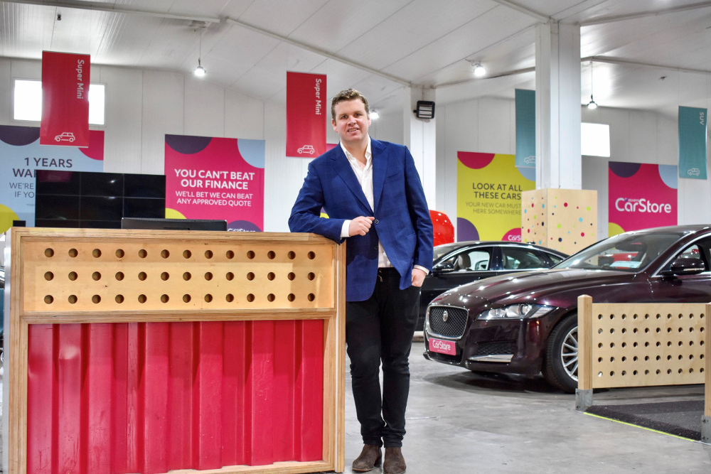 Man in blue jacket standing in motor dealership.