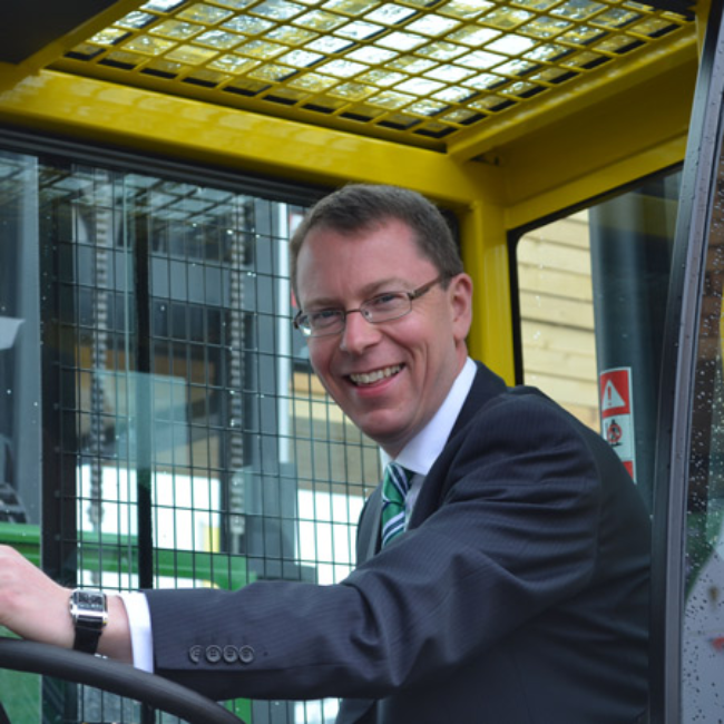 Man in suit behind wheel of a forklift.