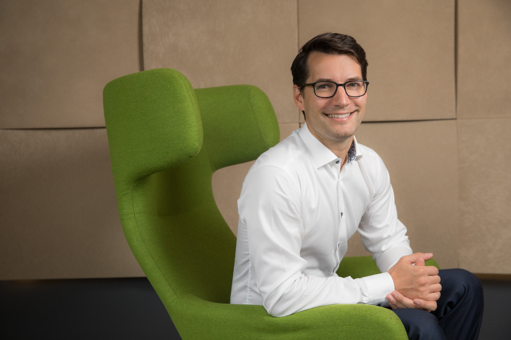 Smiling man in green chair wearing white shirt.