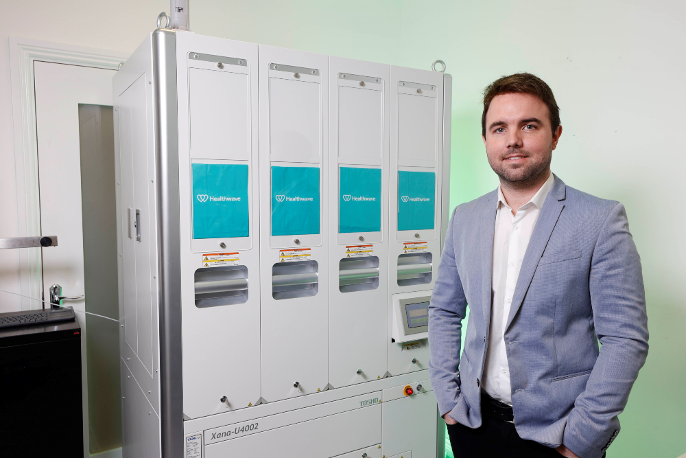 Man in blue jacket standing beside machine.