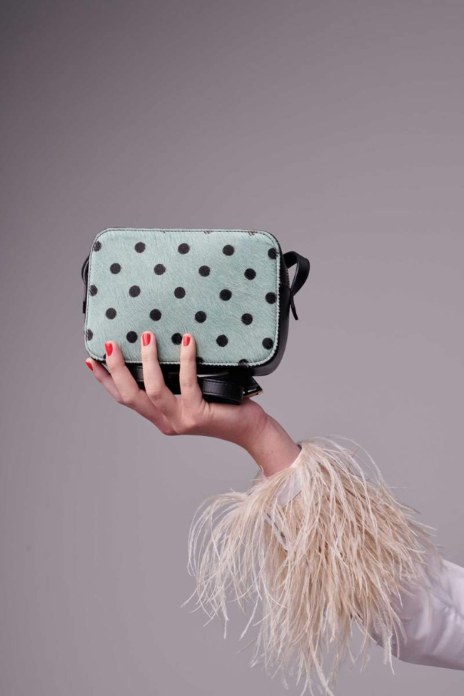 Woman's hand holding a pale blue handbag with spots.