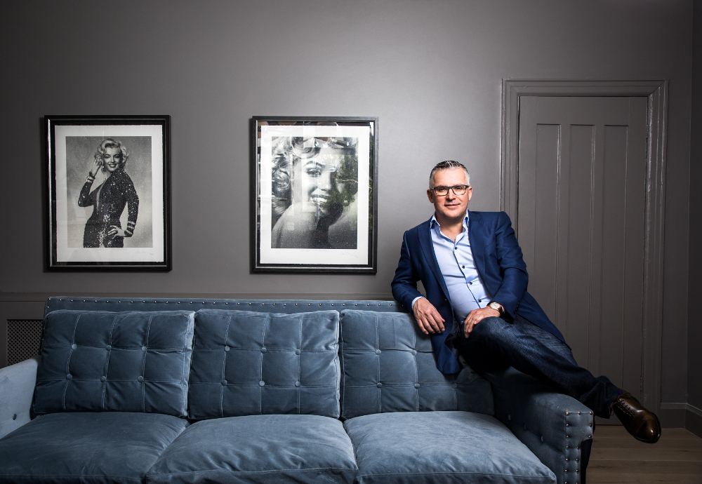 Man in navy jacket leaning on a couch.