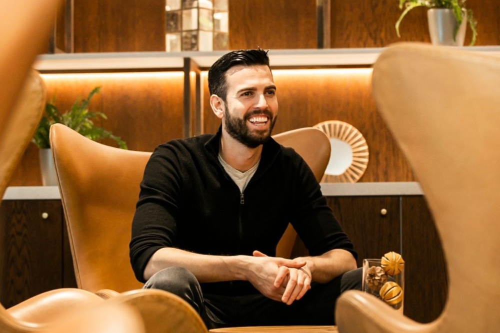 Man in black jumper on tan seat.