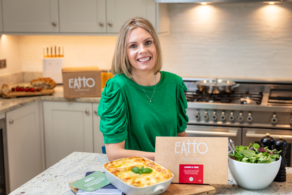 Woman in green top sitting in a kitchen.