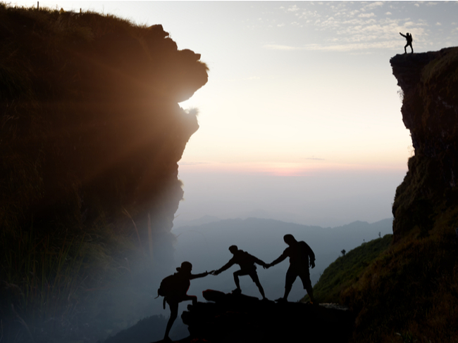 People helping each other up a mountain.