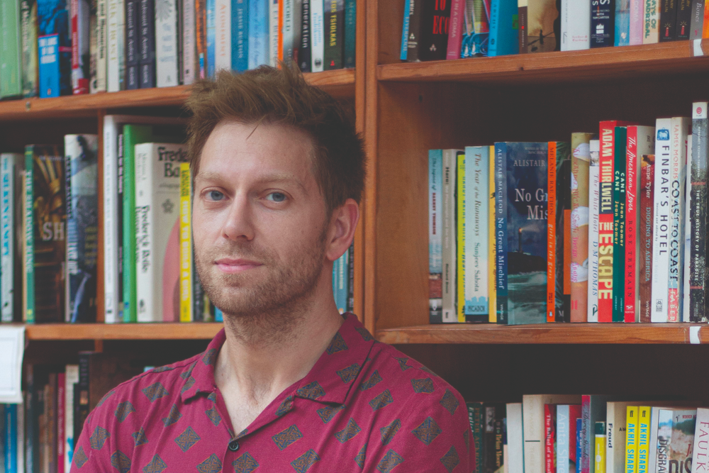 Man in red shirt standing in front of book case.