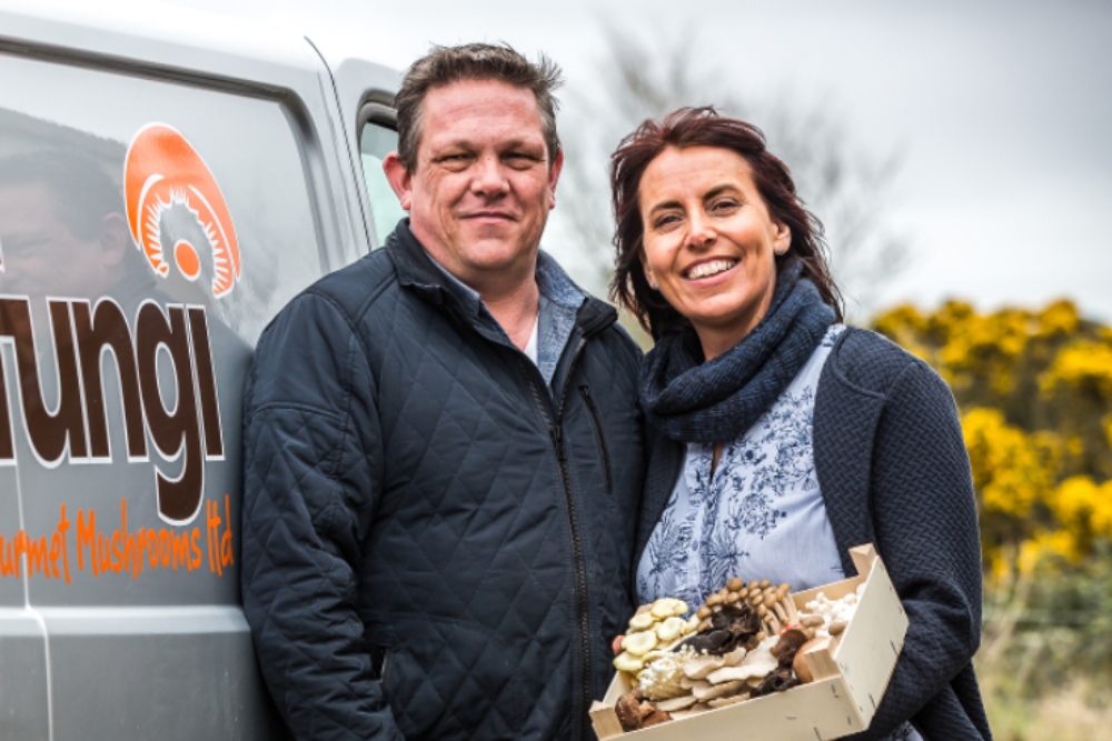 Couple standing beside van holding mushrooms.