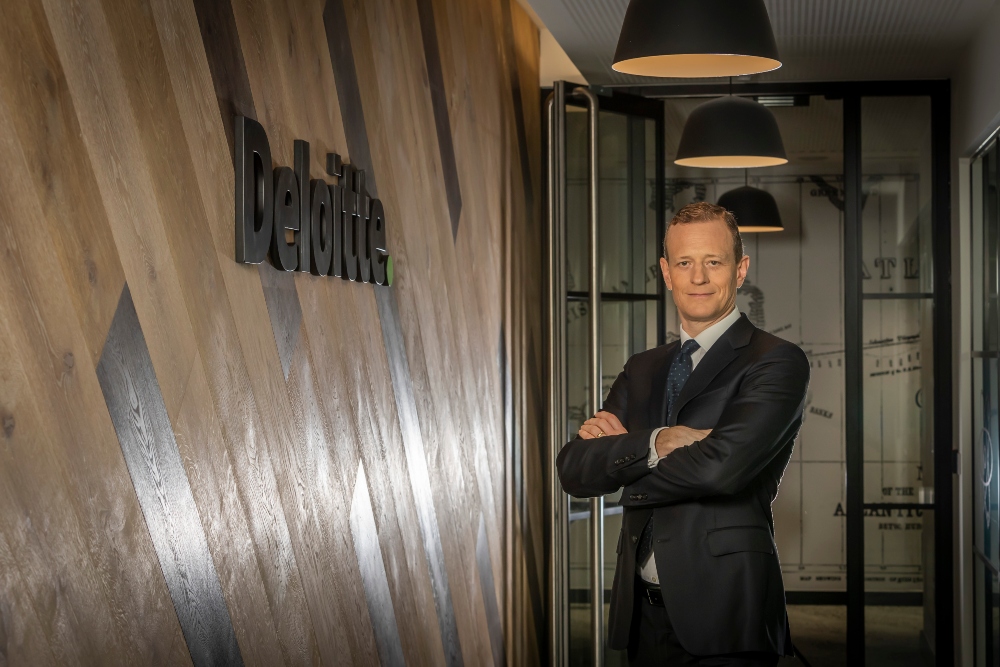 Man in suit beside wall that says Deloitte.