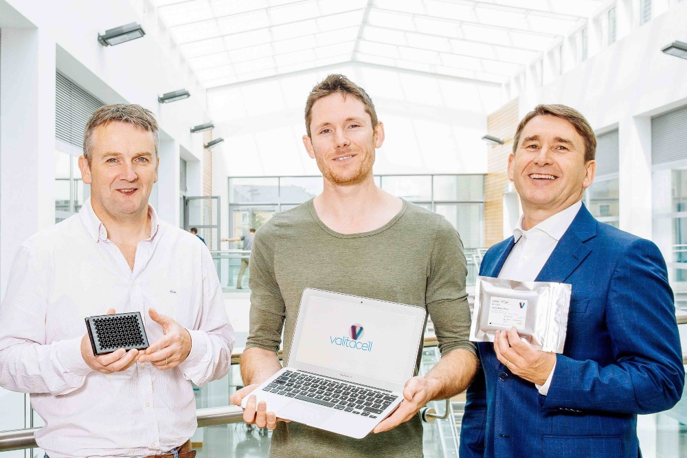 Three men holding biotech products and a computer.