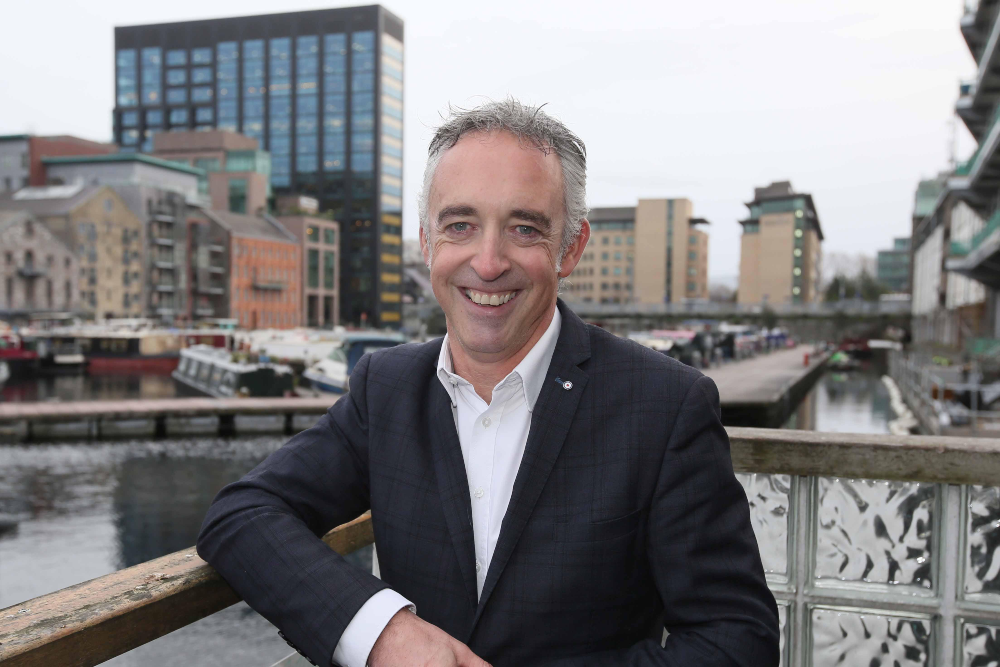 Man in dark jacket standing by canal in Dublin.