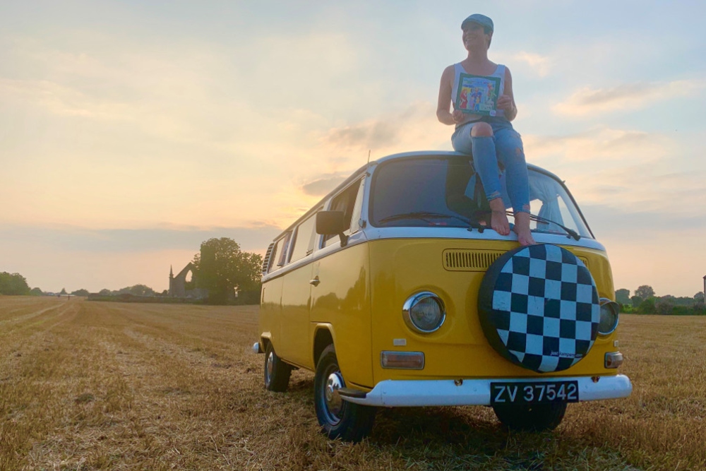 Woman sitting on top of a Volkswagen camper van.