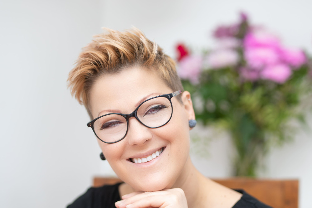 Smiling woman with blonde/red hair and glasses.