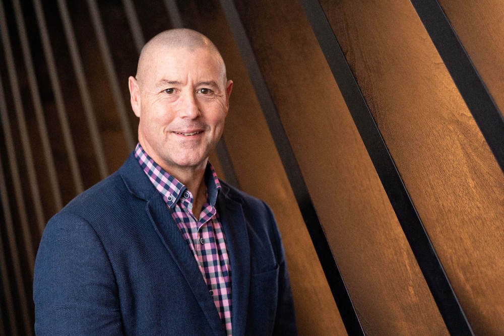 Man in blue jacket in front of wooden wall.