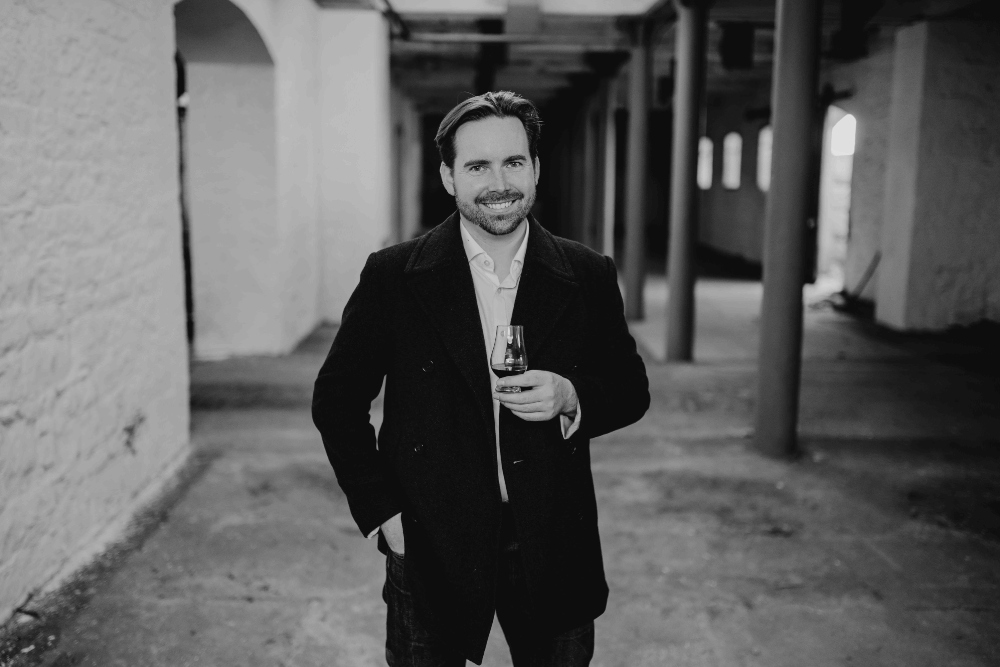 Man in black jacket holding a glass of whiskey.