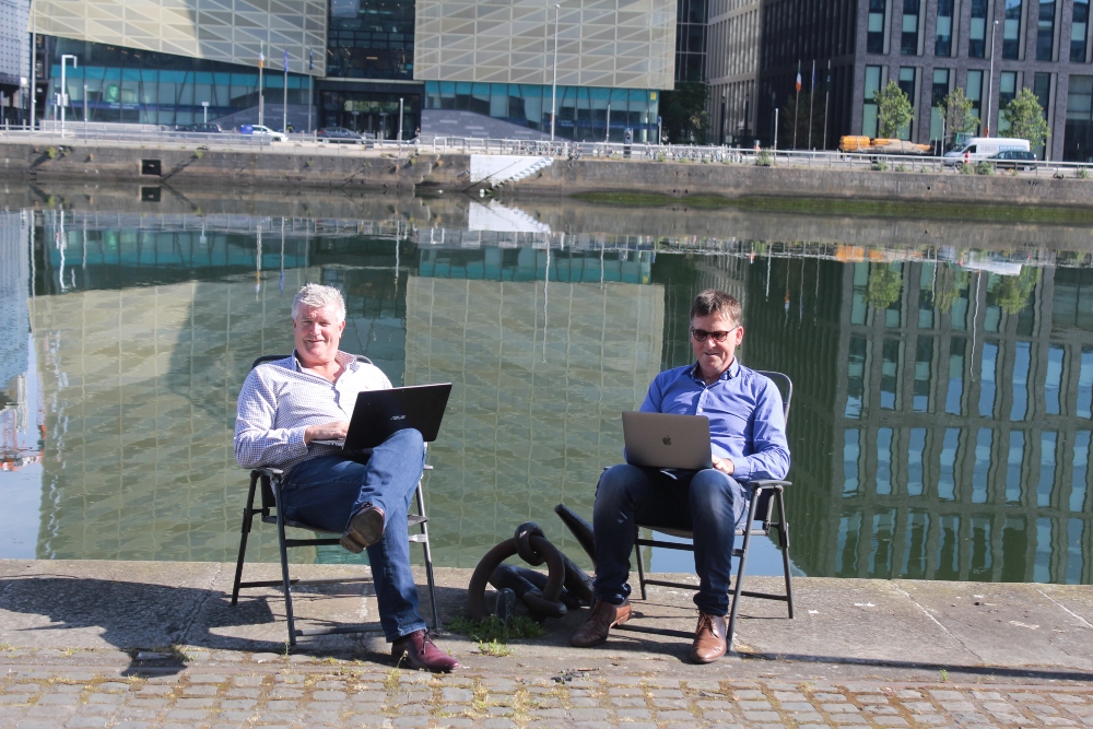 Two men with laptops sitting by the River Liffey.