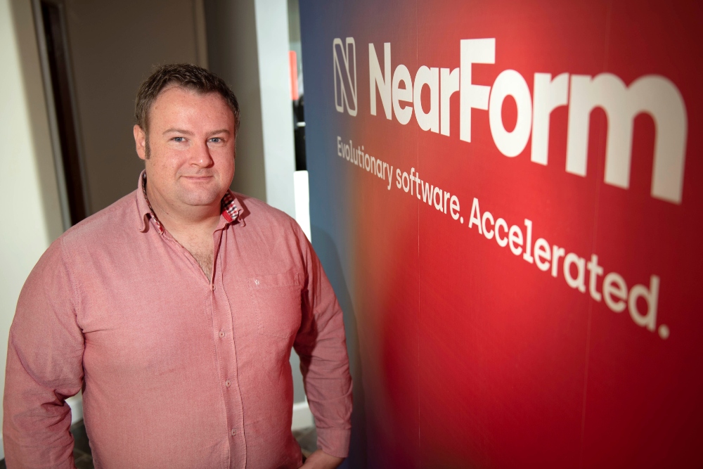 Man in pink shirt standing beside NearForm sign.