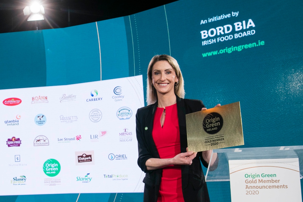 Woman in red dress and black jacket holding up an award.