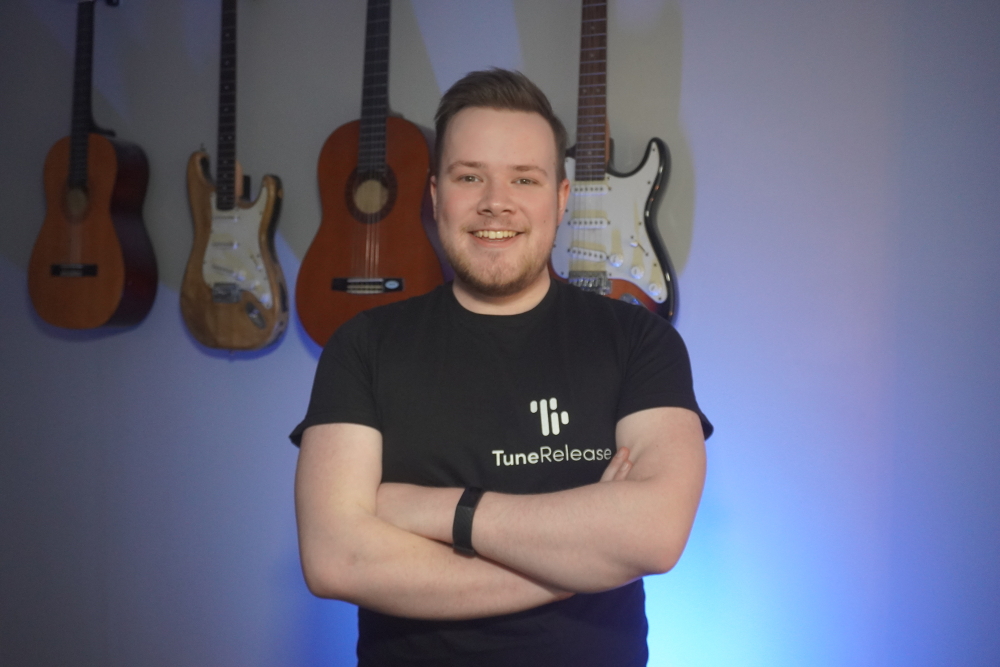 Young man in black t-shirt standing in front of guitars.