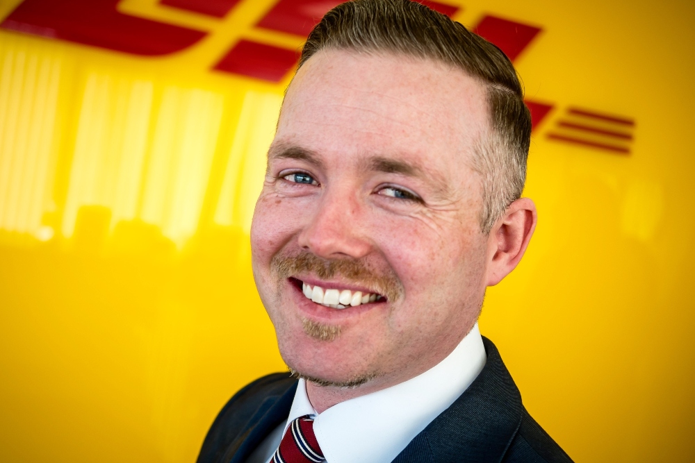 Suited young man in front of DHL branding.