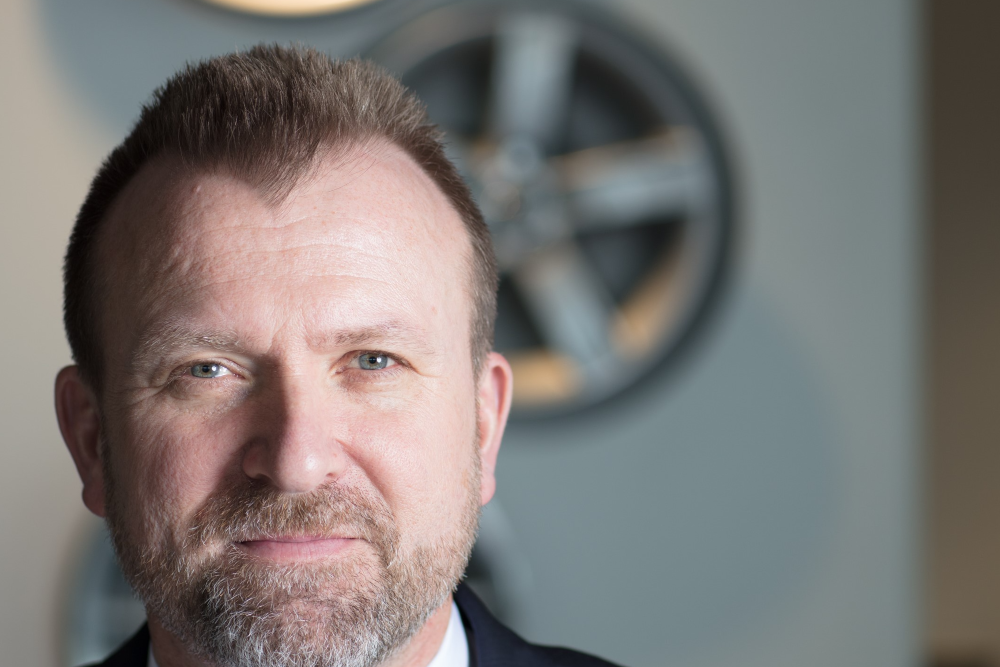 Bearded man standing in front of wheels on a wall.